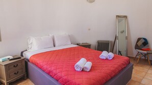 A neatly made bed with a red quilt, two pillows, and two rolled towels.