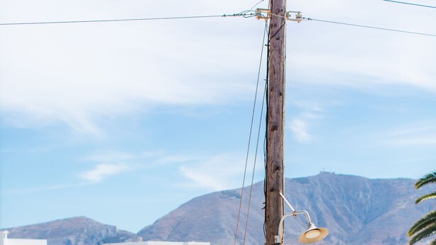 A white building with blue doors and windows, a wooden utility pole, and a mountainous landscape in the background.