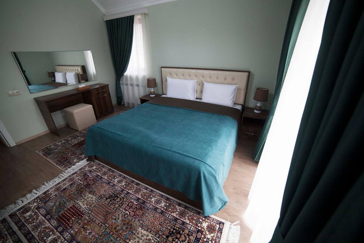 Una habitación de hotel con una cama grande, un aparador, un espejo y un tapete estampado.