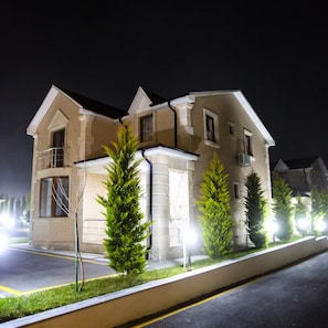 A two-story house with a brick facade, a balcony on the second floor, and a small front yard with two evergreen trees. - AlmaBagi Hotel&Villas (Quba)