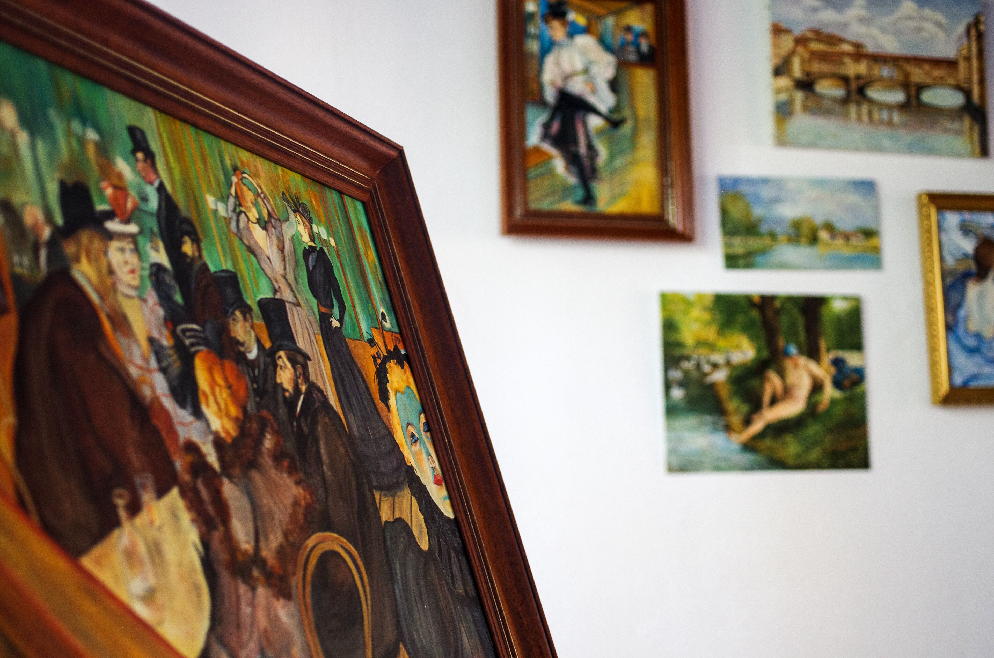 A wall with various framed artworks, including a large painting of a group of people and smaller landscape paintings.