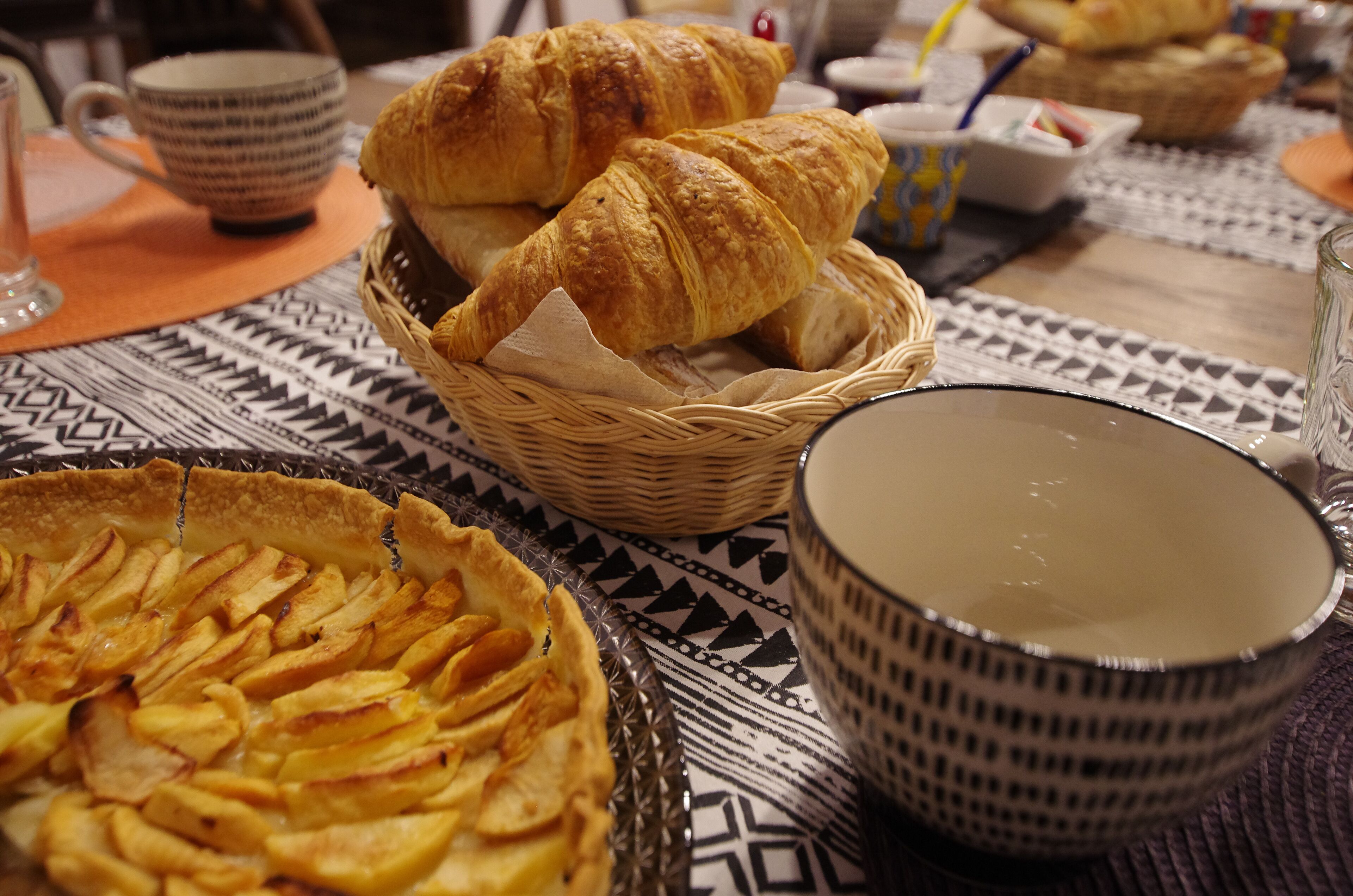 Una mesa con un pastel, cruasanes y un bol.
