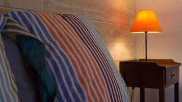 Una cama con almohadas a rayas y un cabecero de madera, una mesita de noche con una lámpara, y una pared de madera.
