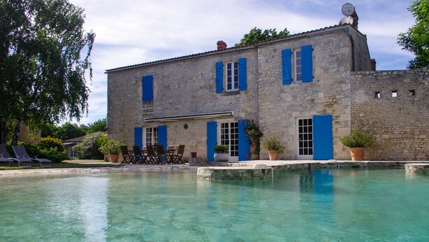 A stone building with blue shutters and a clear pool in front.