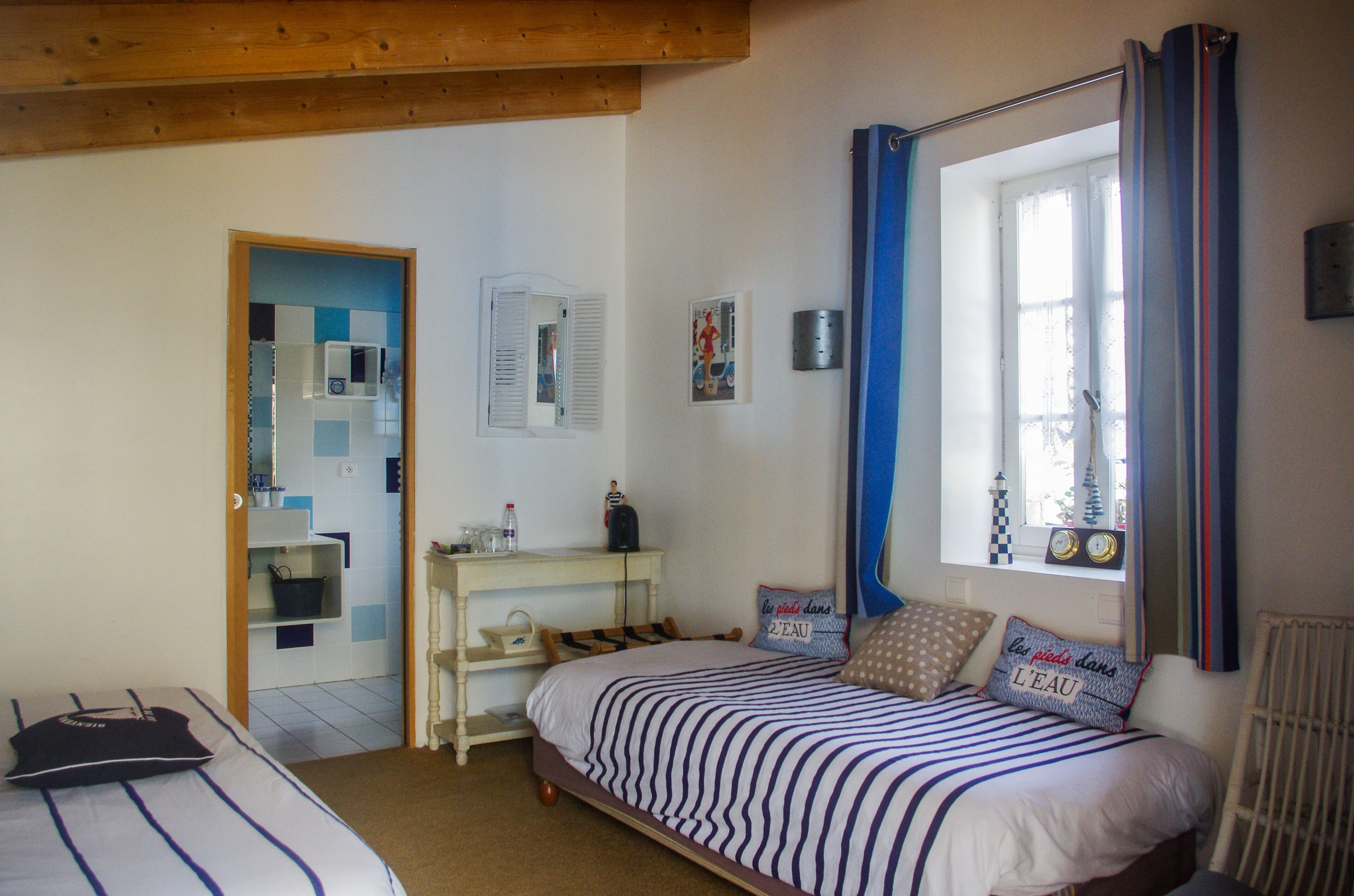 Une chambre à coucher avec un lit, une fenêtre avec des rideaux, une petite table avec une lampe et une étagère avec des articles de toilette.