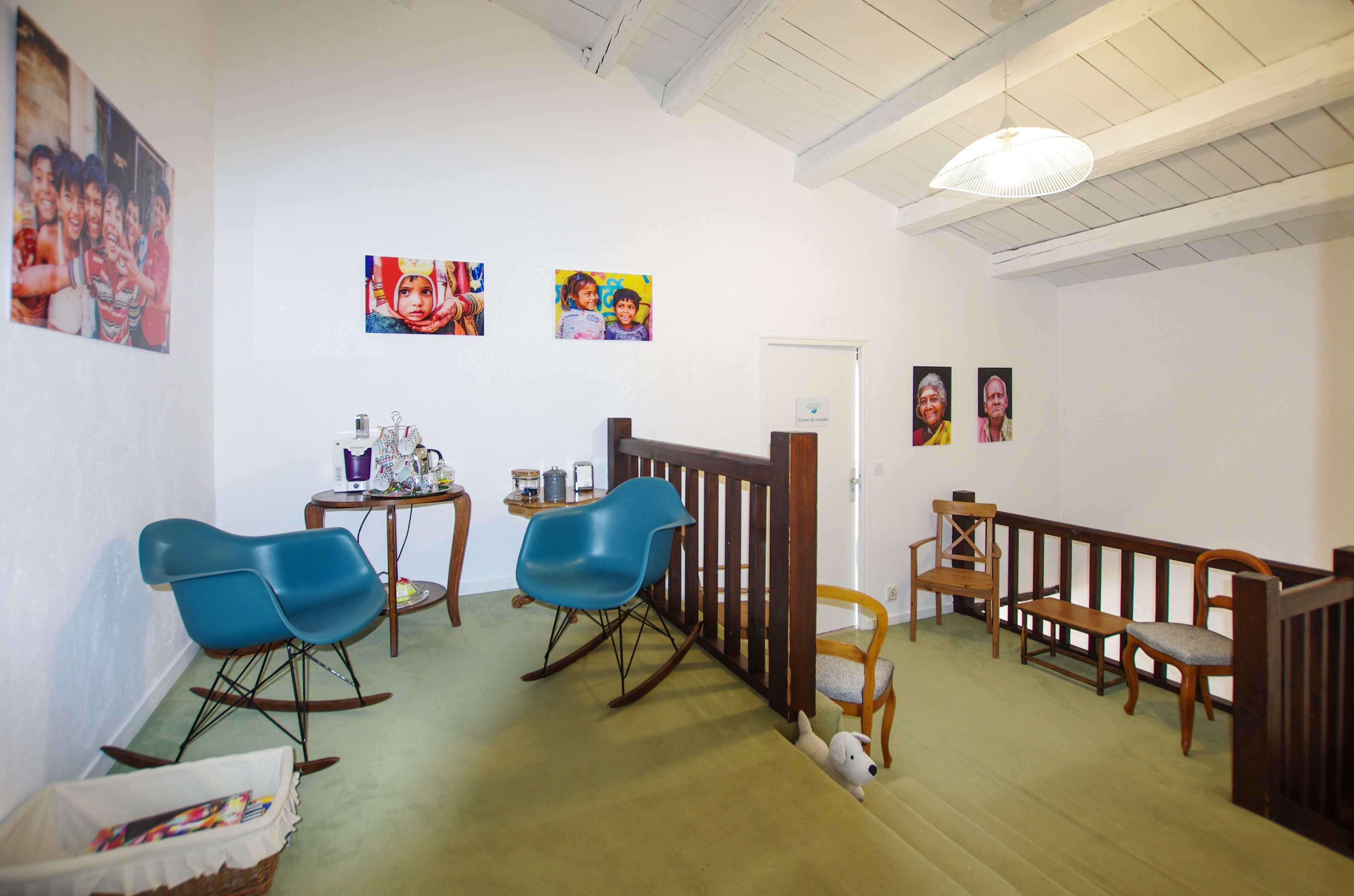 A room with a wooden bench, a rocking chair, and a blue chair. There are pictures on the wall and a door with a sign.