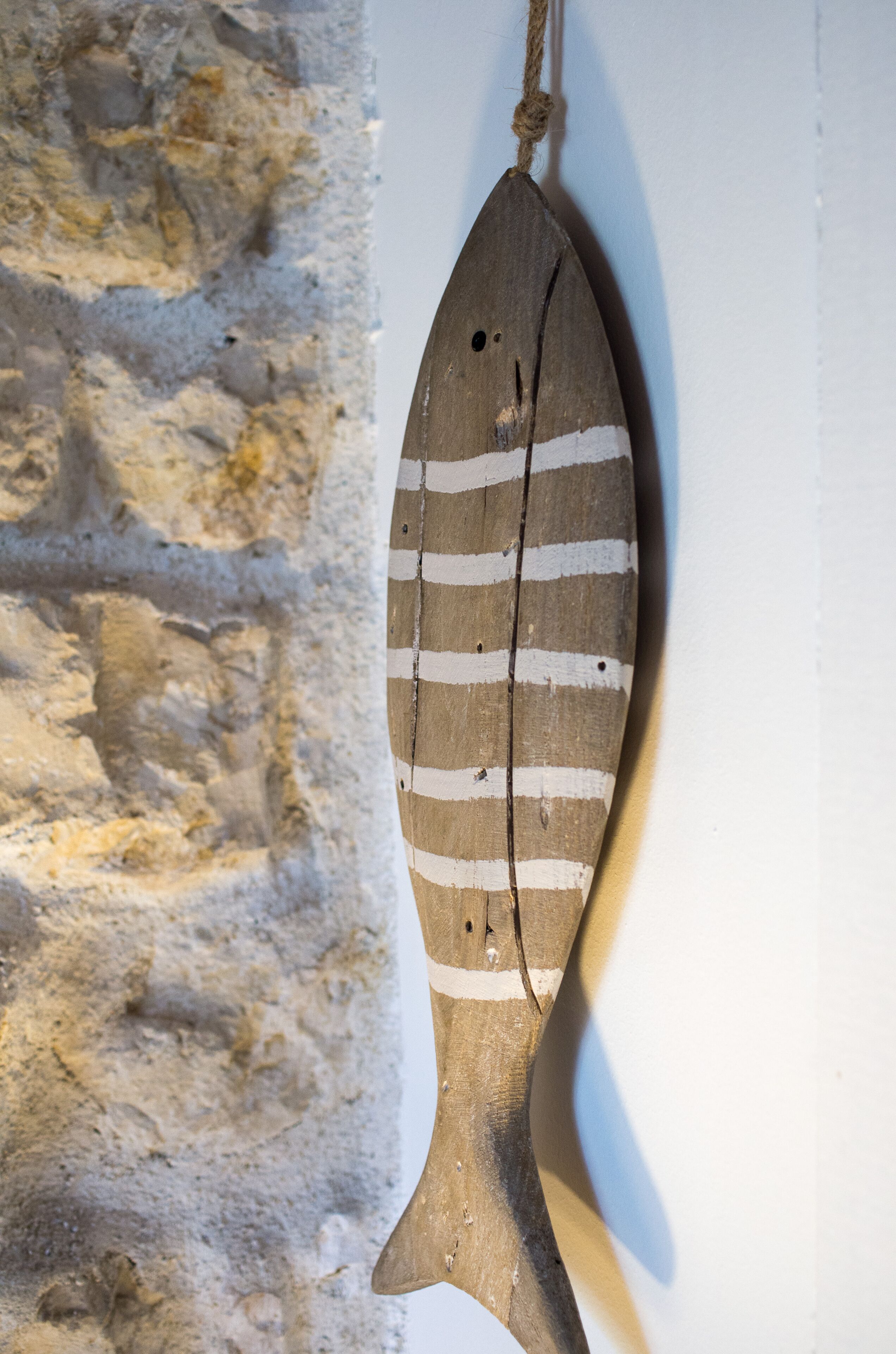 A wooden fish decoration with stripes, hanging on a wall with a textured stone background.