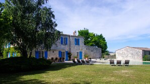 A stone building with blue shutters, a pool, and outdoor seating.