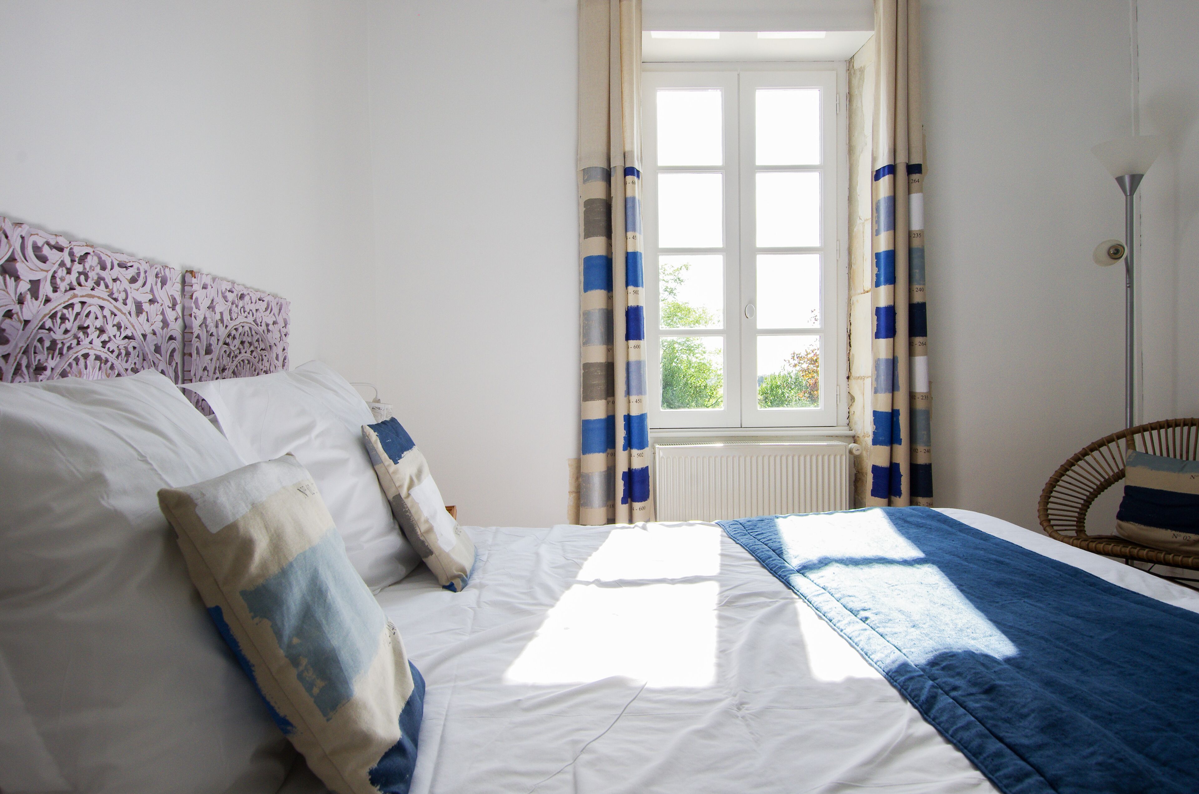 Ein Schlafzimmer mit Bett, Vorhängen, einem Fenster und einem Sessel.