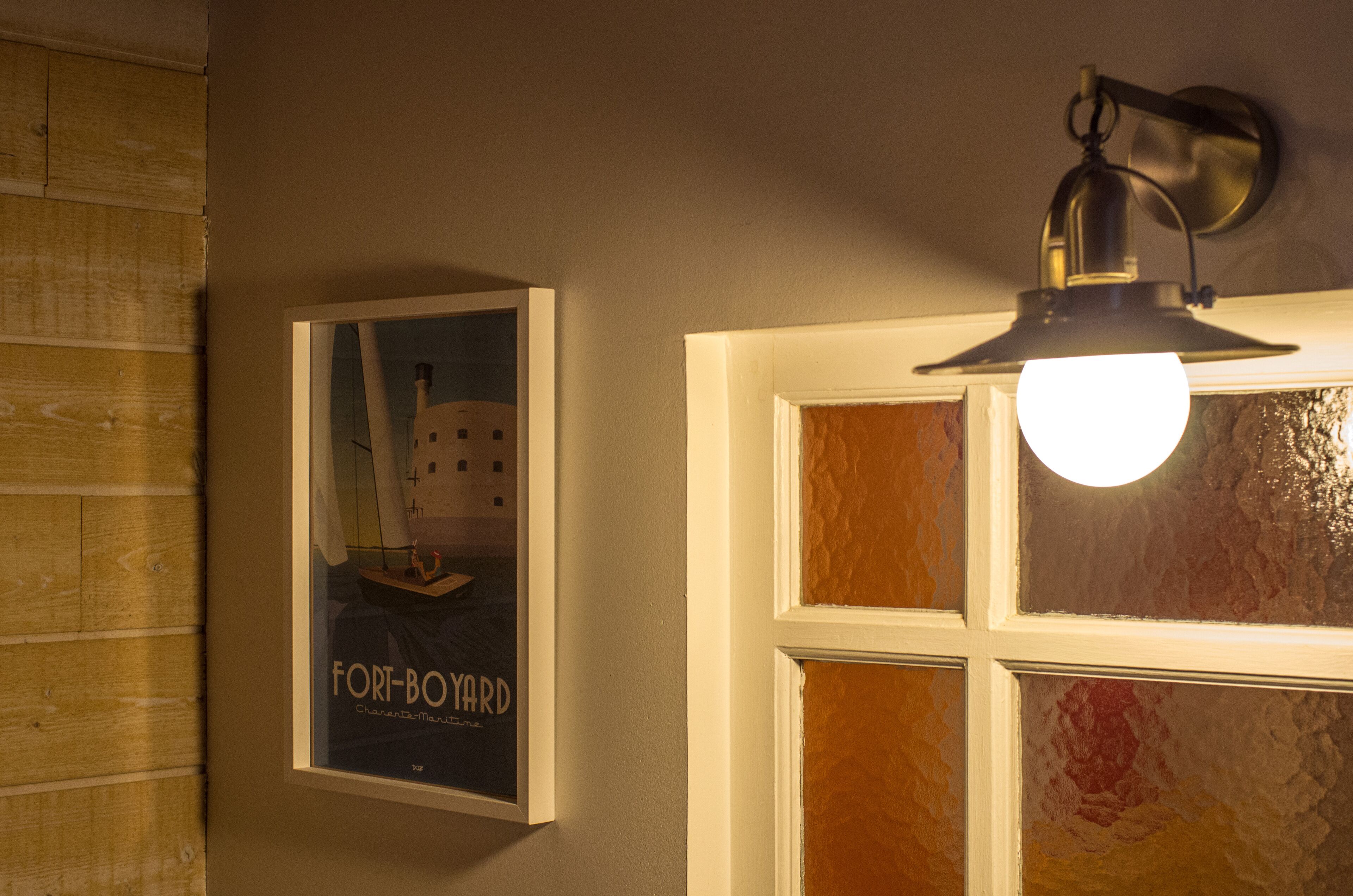 Un cartel enmarco con un velero en una pared, una ventana con lámpara y paneles de madera.