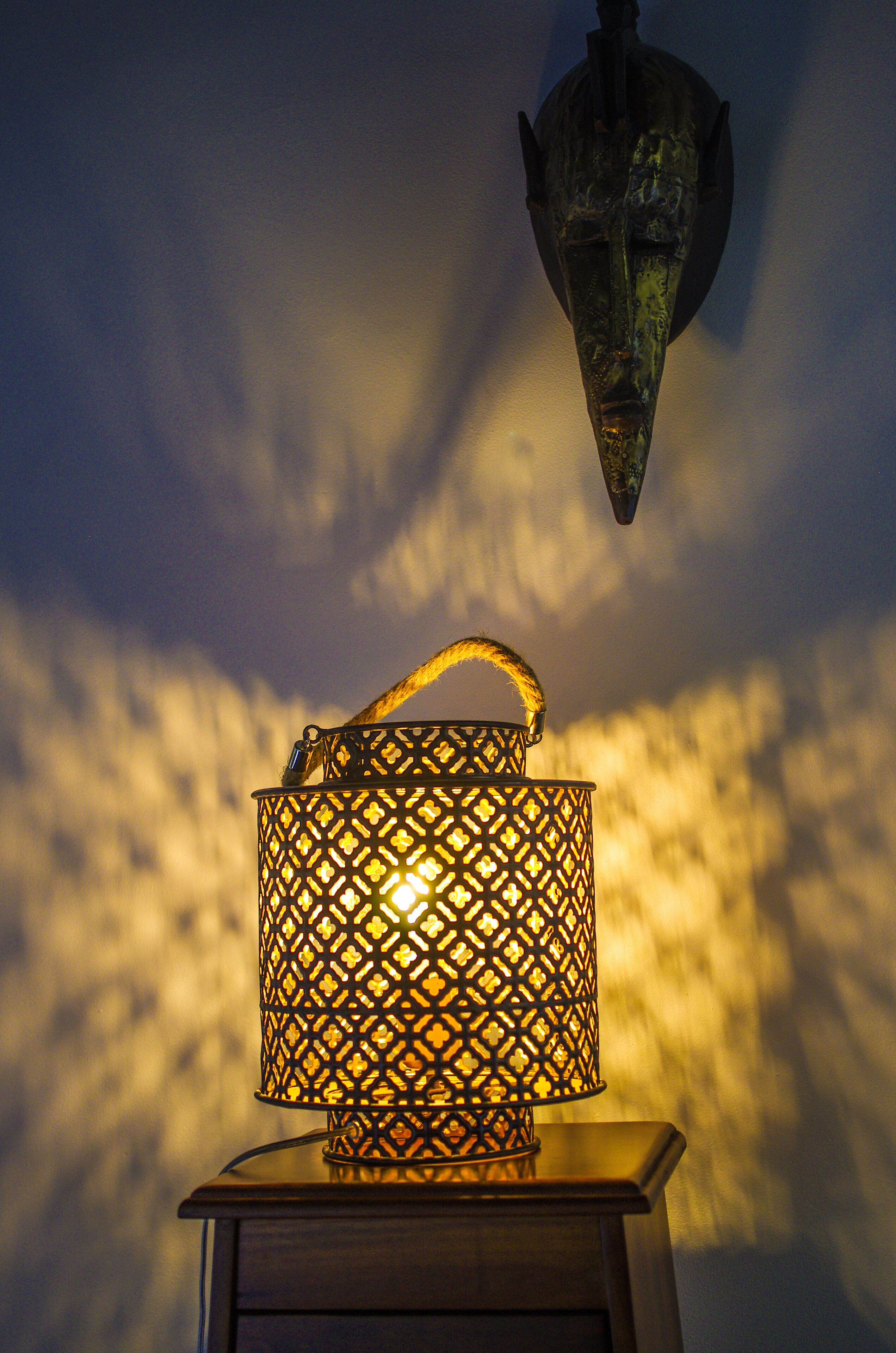 A wall-mounted lantern with a handle, casting a warm glow against a textured wall.