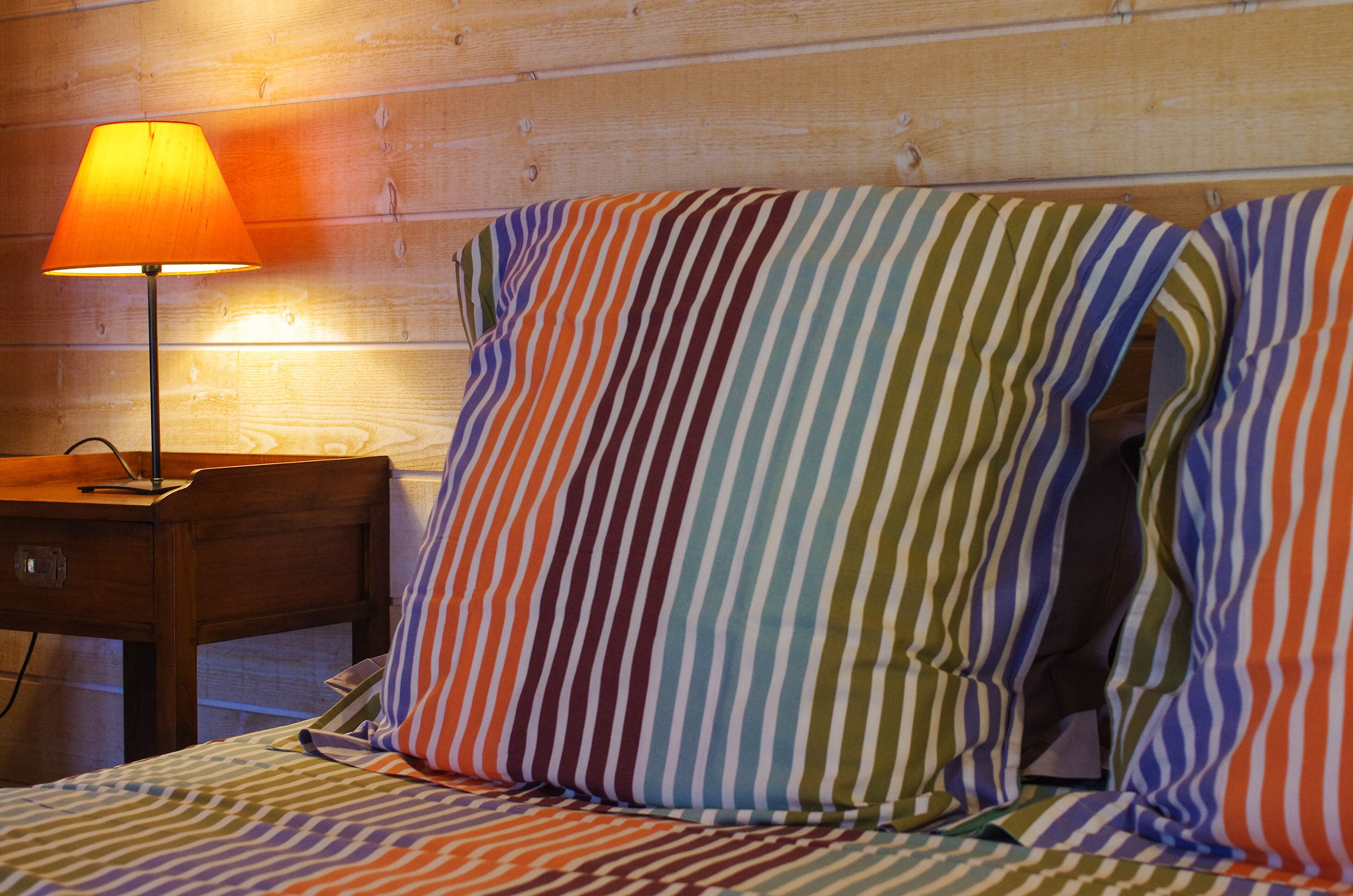 A bed with striped bedding and a nightstand with a lamp.