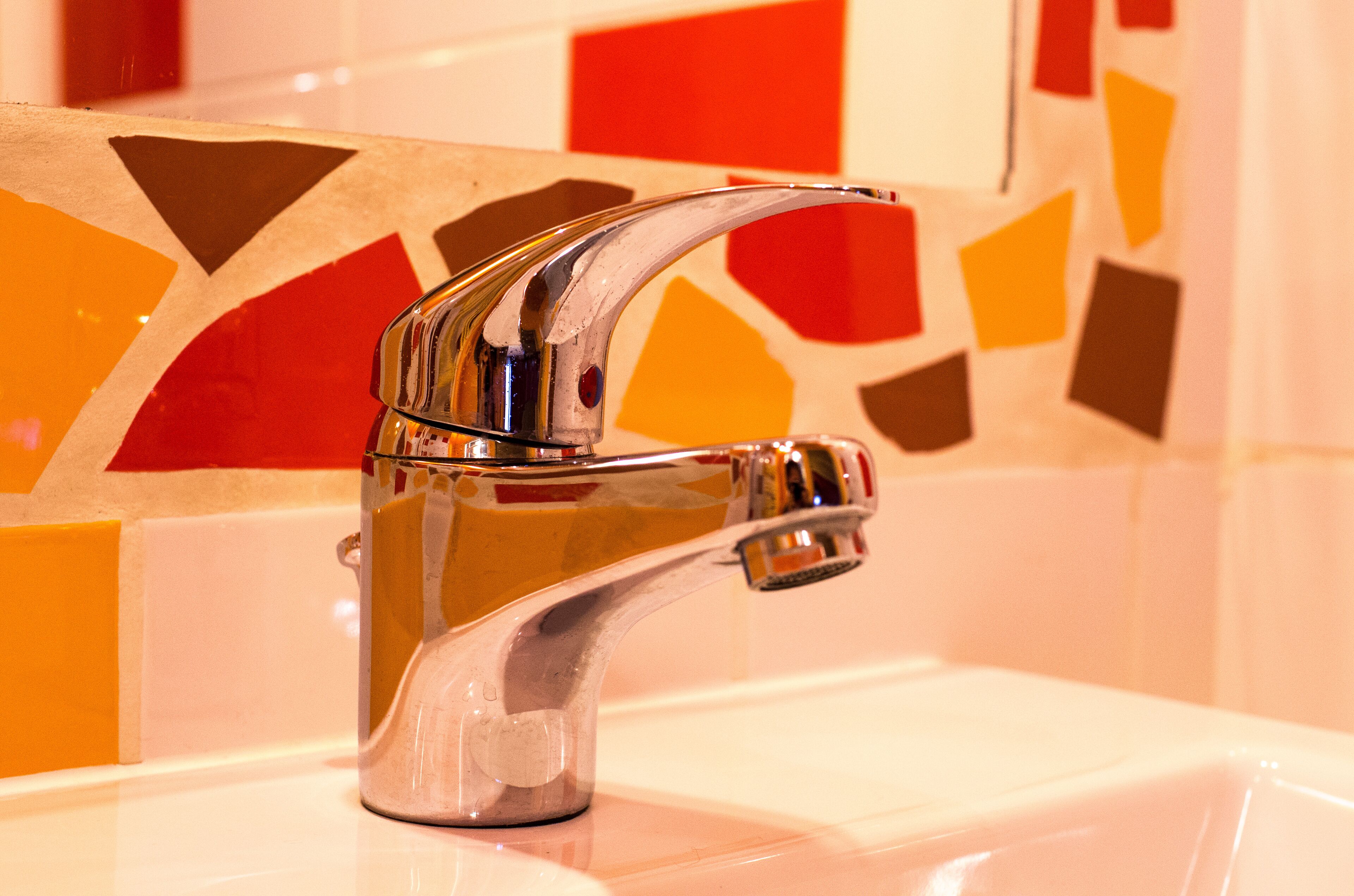 Een badkamer met een chromen kraan en een betegelde muur met geometrische patronen.