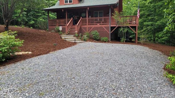 A two-story wooden cabin with a porch, surrounded by a gravel driveway and lush greenery. - Peaceful Blue Ridge Mountain Retreat Near Marion, NC (Nebo)