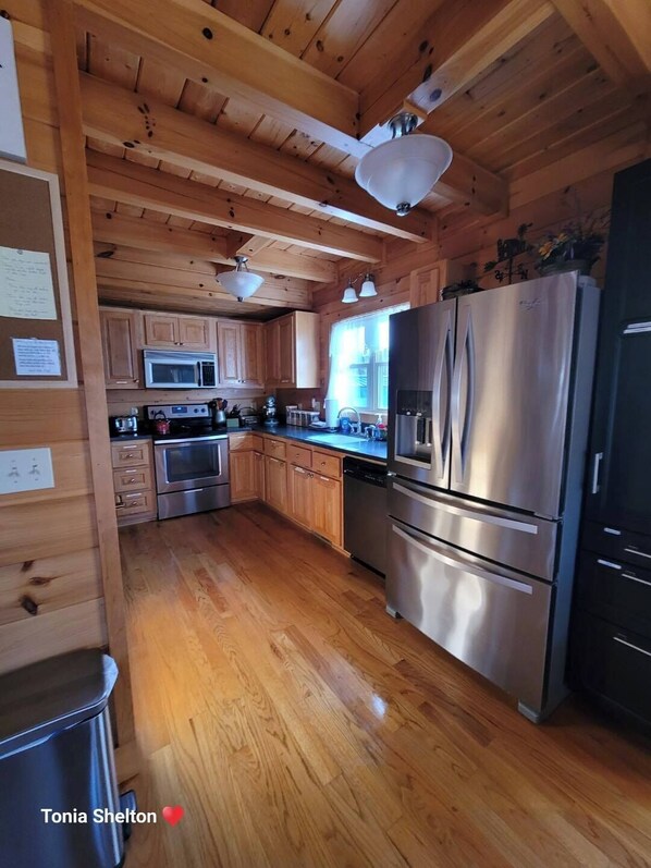 A wooden cabin kitchen with a stainless steel refrigerator, oven, microwave, and a sink.