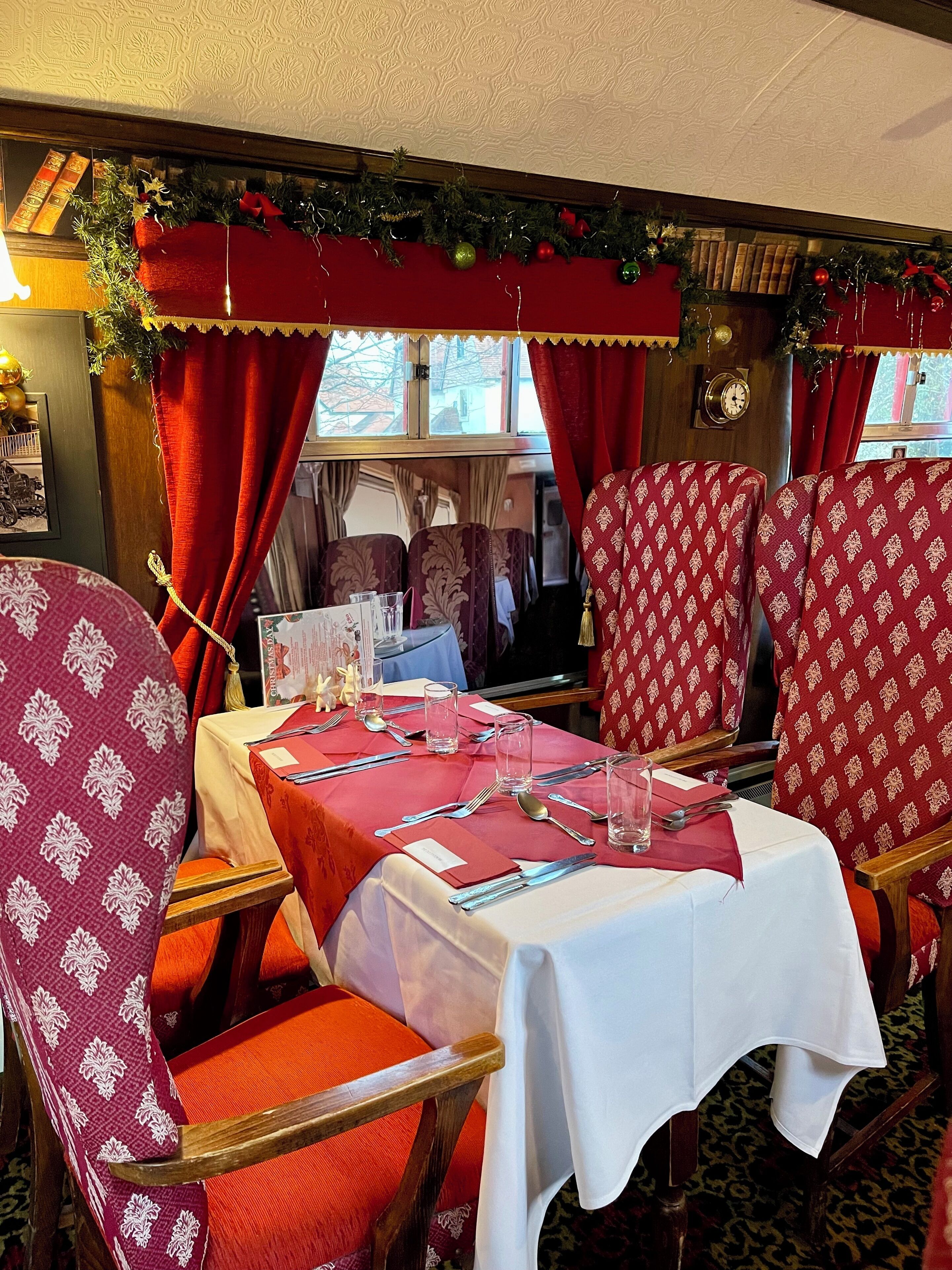 Uma sala de jantar com cadeiras de padrão vermelho e branco, uma mesa posta com talheres e copos, e decorações de Natal.
