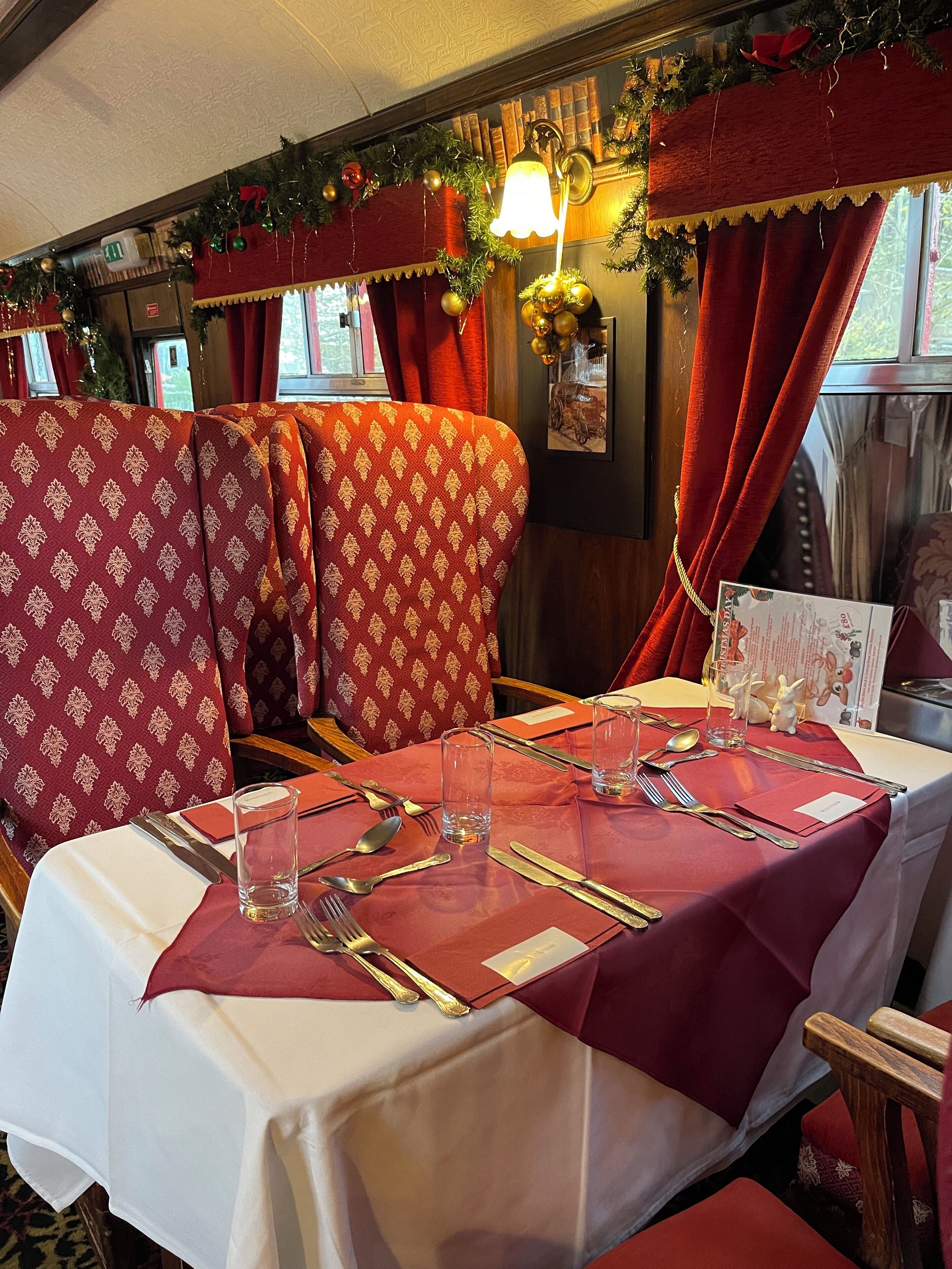 Un coin repas avec des chaises à revêtement rouge, une table dressée avec des couverts et des verres, et un menu posé sur la table.