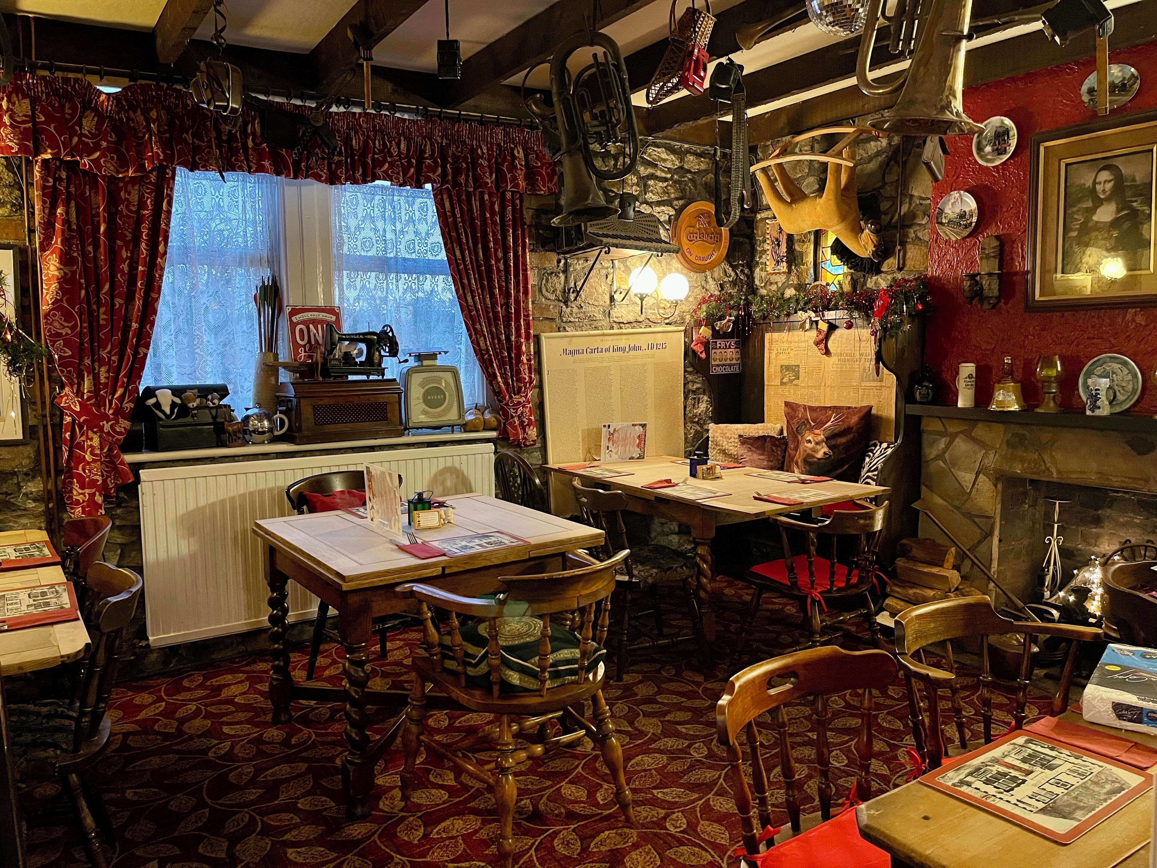 A cozy dining area with a table set for two, surrounded by wooden chairs. A vintage sewing machine and a typewriter are visible on the windowsill.