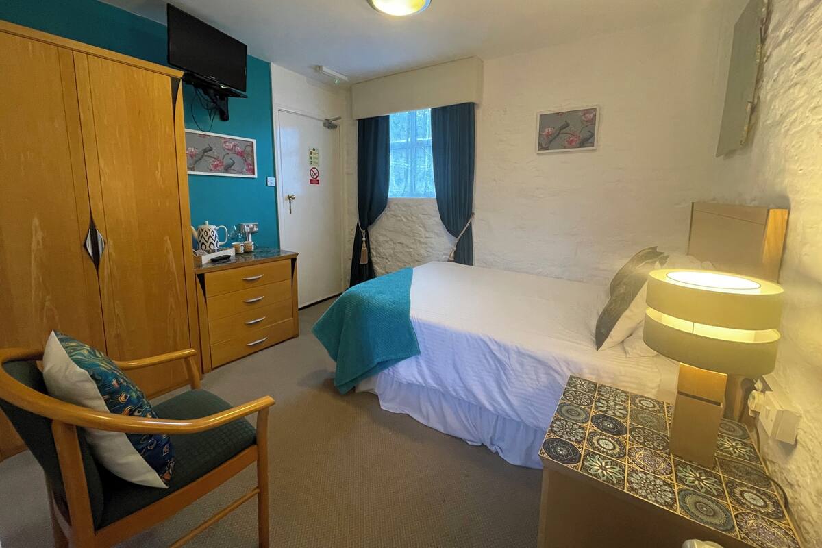 A hotel room with a bed, a desk with a lamp, a chair, a wardrobe, and a television on the wall.