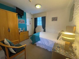 A hotel room with a bed, a desk with a lamp, a chair, a wardrobe, and a television on the wall.