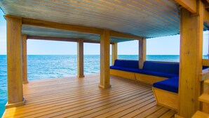 A wooden deck with blue cushioned seating and a view of the ocean. - Tortuga Terrace-43 Lawson Rock 3 Bedroom Home by RedAwning (Roatan)
