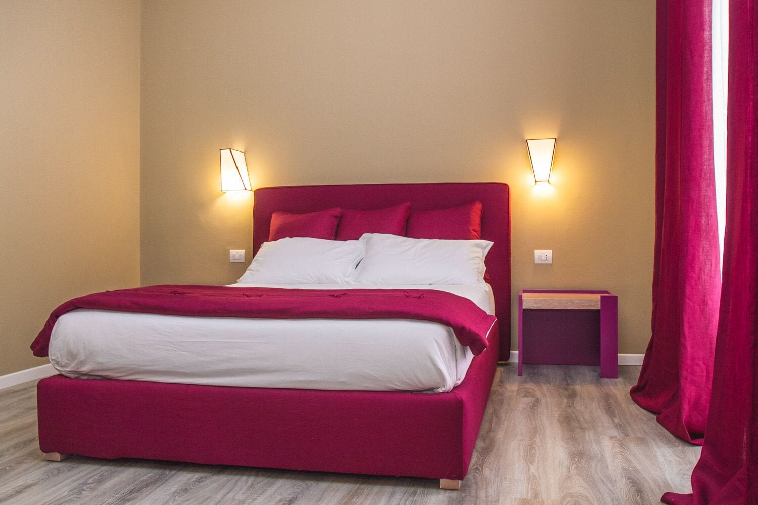 Un letto con testiera rossa e biancheria bianca, due comodini e un pavimento in legno.