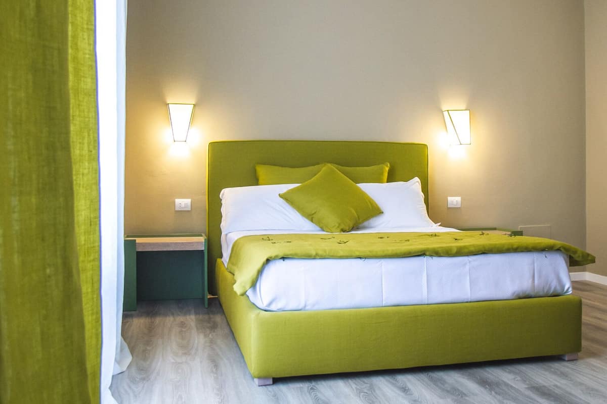 A bed with a green headboard, white bedding, and a green throw blanket. There are two wall-mounted light fixtures on either side of the bed.
