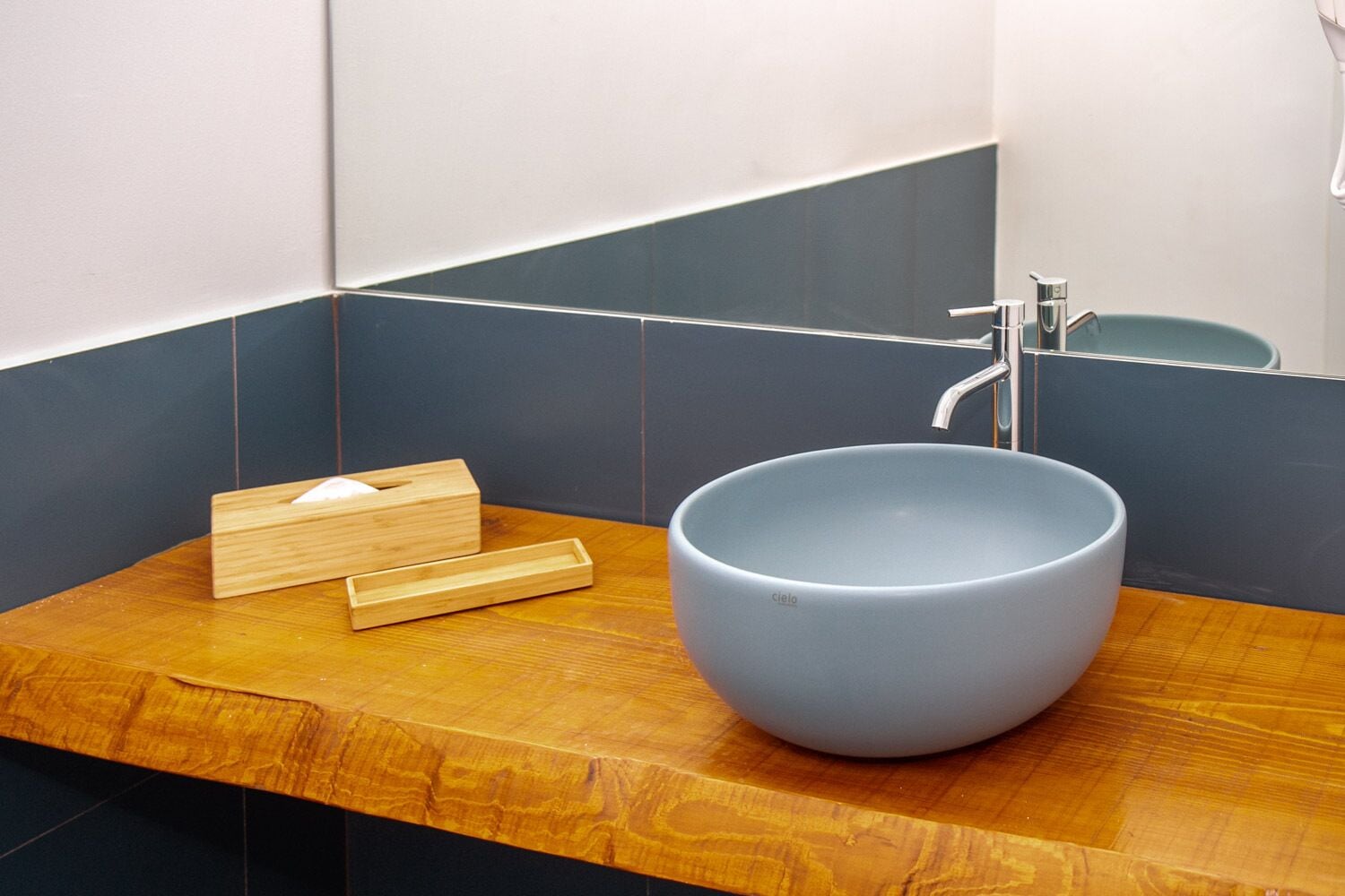 A bathroom with a wooden vanity, a large blue basin, and a wooden tissue box.