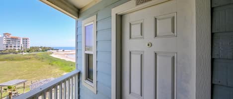 Una puerta blanca con el número 2314, un balcón con barandilla y vista a una playa y edificios a lo lejos.