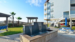 A pool area with a water feature, picnic tables, and a building with balconies.