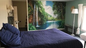 Hotelkamer met een groot bed, nachtkastje, lamp, stoel, bureau en een muurschildering van een waterval.