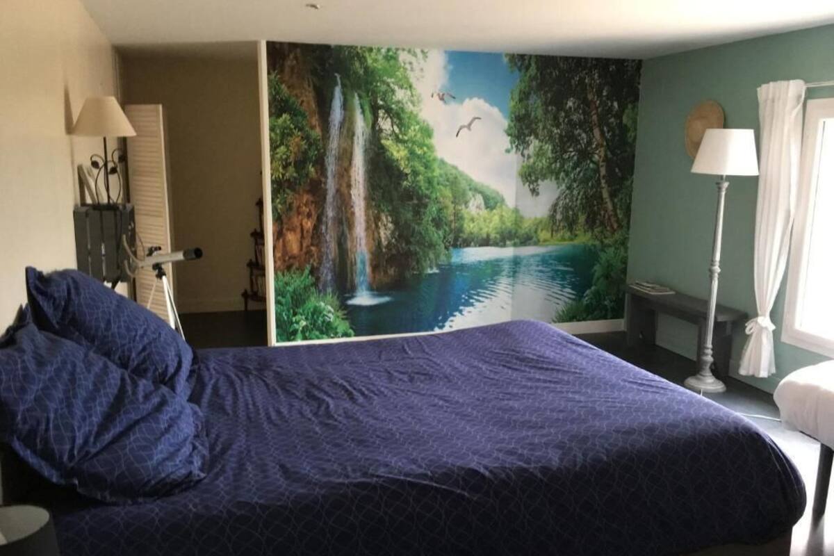 Una habitación de hotel con una cama grande, una mesita de noche, una lámpara, una silla, un escritorio y un mural de una cascada.