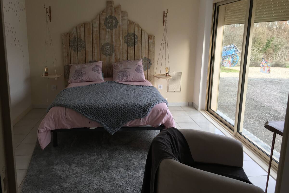 Un dormitorio con una cama, dos mesitas de noche, una lámpara colgante, una ventana y una silla.