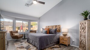 A bedroom with a large bed, a wooden headboard, a nightstand, a dresser, and a window with a view of the outside. - Mystic Mirage is truly a desert oasis with pool and mountain views. (Tucson)