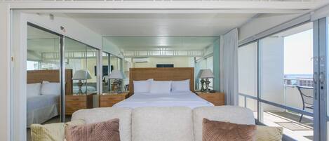 Une chambre d’hôtel moderne dotée d’un grand lit, d’un canapé avec des coussins, d’un balcon offrant une vue agréable et d’un grand miroir qui reflète la pièce.