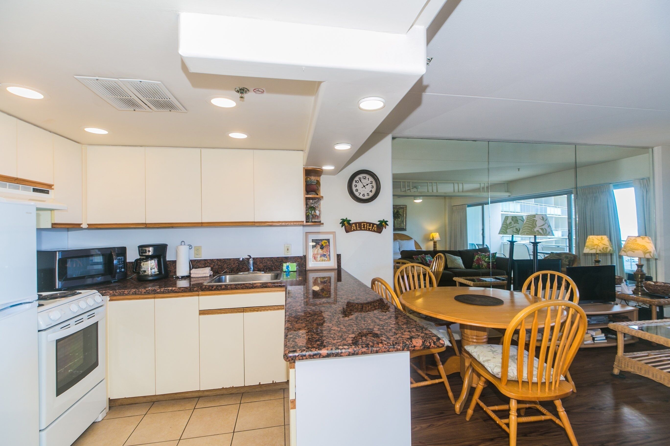 A kitchen with white cabinets, a granite countertop, a microwave, a stove, and a dining area with a wooden table and chairs.