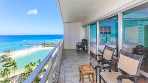 A balcony with a view of a beach and ocean. There are two chairs and a small table.