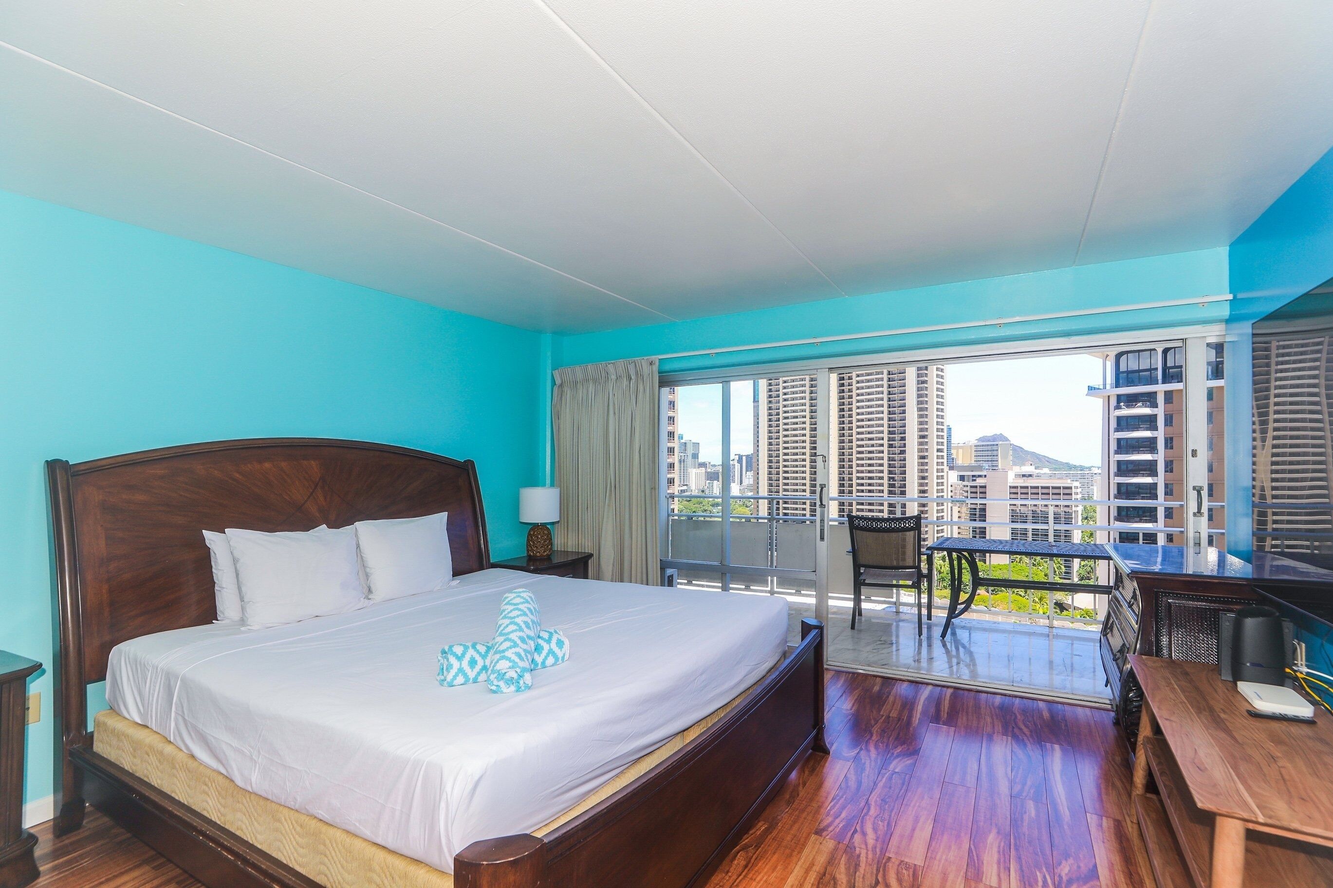 A hotel room with a large bed, a desk, and a balcony with a city view.