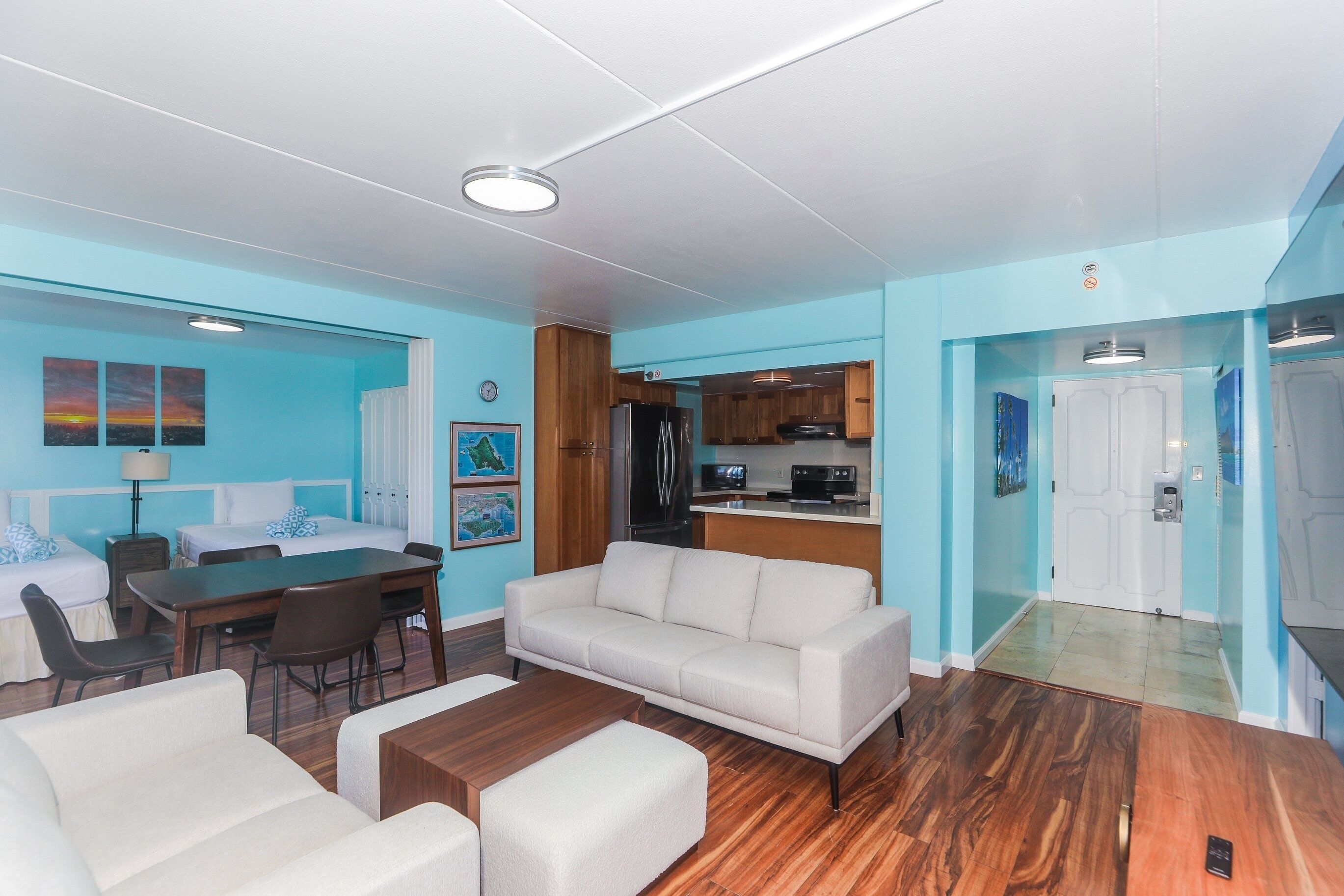 A modern hotel room with a dining area, a sofa, a coffee table, and a kitchen area.