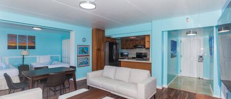 A modern hotel room with a dining area, a sofa, a coffee table, and a kitchen area.