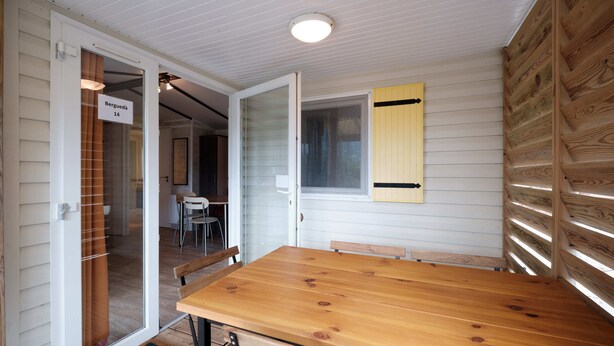 Ein Holztisch mit Stühlen, eine Schiebetür aus Glas und ein Fenster mit Jalousien.