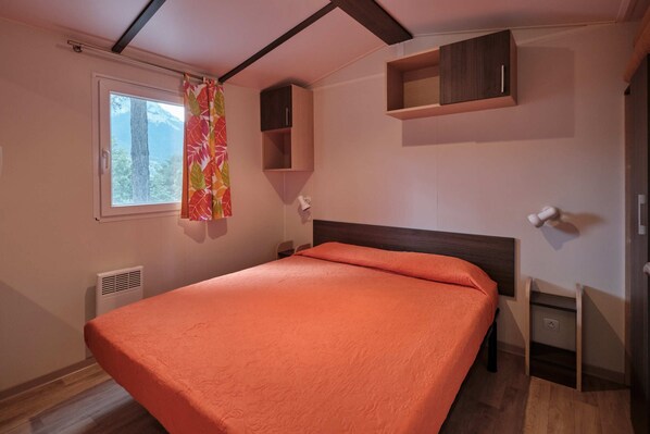 A bedroom with a bed, a window with curtains, a bedside table, and built-in shelves.