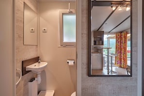 A modern bathroom with a sink, mirror, and toilet. It features a window with frosted glass and a view of a balcony with a colorful curtain. - Camping Repòs del Pedraforca (Saldes)