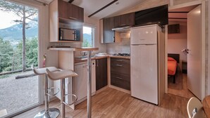 A modern kitchen with a view of the outdoors, a refrigerator, a stove, and bar stools. - Camping Repòs del Pedraforca (Saldes)