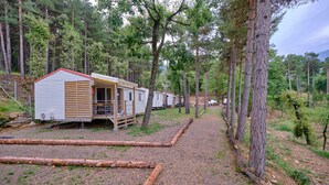 A row of mobile homes in a wooded area with a gravel path. - Camping Repòs del Pedraforca (Saldes)
