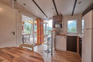 A modern kitchen with a wooden table, bar stools, a dishwasher, and a view of the outdoors.