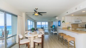 A spacious living area with a balcony overlooking the ocean, a dining area with a round table and chairs, and a kitchen with white cabinets and a microwave. - Two Bedroom Condo Overlooking Ala Wai Boat Harbor by RedAwning (Honolulu)