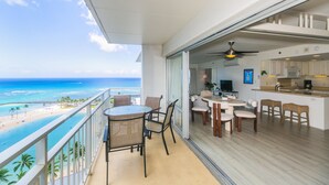 A balcony with a view of the beach and ocean, a dining area with chairs and a table, and a kitchen with a counter and appliances. - Two Bedroom Condo Overlooking Ala Wai Boat Harbor by RedAwning (Honolulu)