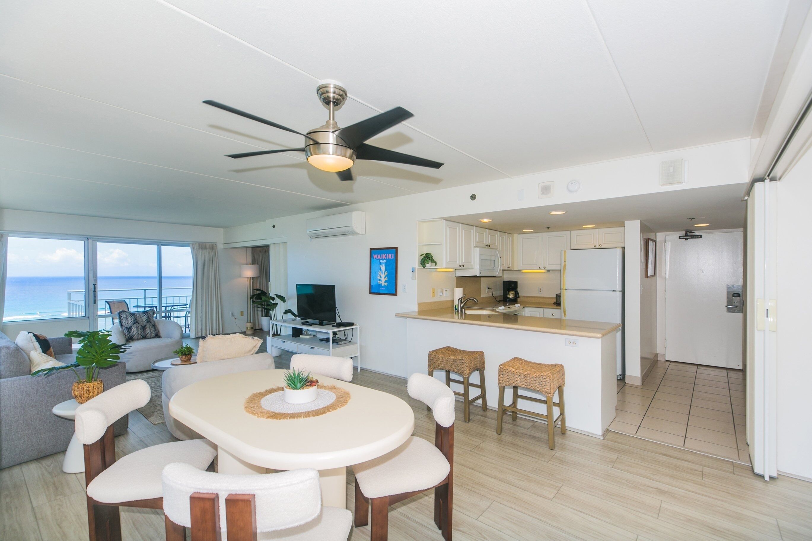A modern living room with a dining area, kitchen, and a balcony with a view of the ocean.