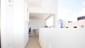 A narrow hallway with white walls and a beige floor, leading to a room with a window and a small plant. - Condominio La Dolce Vita (Playa del Carmen)